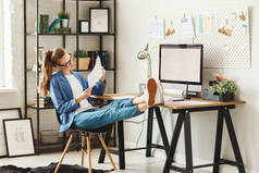 Optimistic young busy female in casual wear looking at camera while sitting at table with computer a