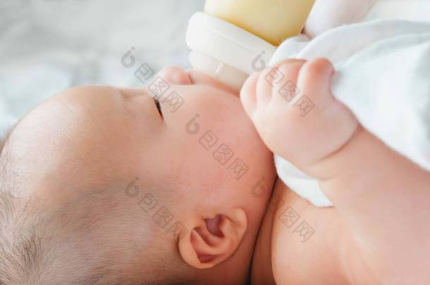 一个亚洲新生儿躺在床上喝着一瓶牛奶，四个月大的迷人的黑眼睛婴儿躺在床上，一个孩子躺在床上