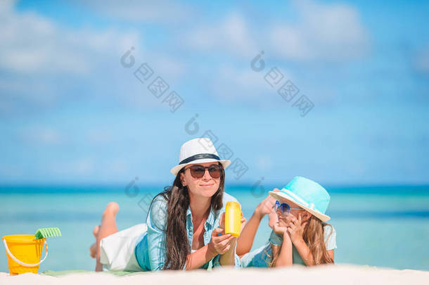 妈妈在<strong>炎炎夏日</strong>把防晒霜放在海滩上的小女儿身上