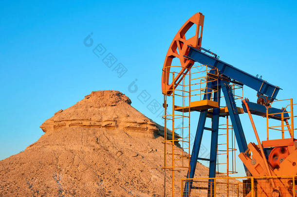 油泵在蓝天的背景下工作.世界石油工业。哈萨克斯坦<strong>西部</strong>地区：油泵是油井内往复式活塞泵的地面驱动装置.