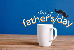 白色的杯子和黑色的装饰纸在木制的表面上挂着假胡子，用蓝色快乐的父亲节的图画隔开