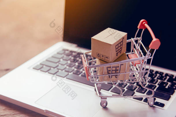 网上购物概念-在笔记本电脑键盘上的推车上有购物车标识的包裹或纸箱。网上购物服务。提供上门送货服务