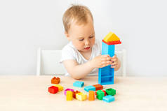 一个2岁的男孩坐在一张桌子旁，有着白色孤立的背景，他收集了一个构造函数，一个早期的发展，一个文本的地方