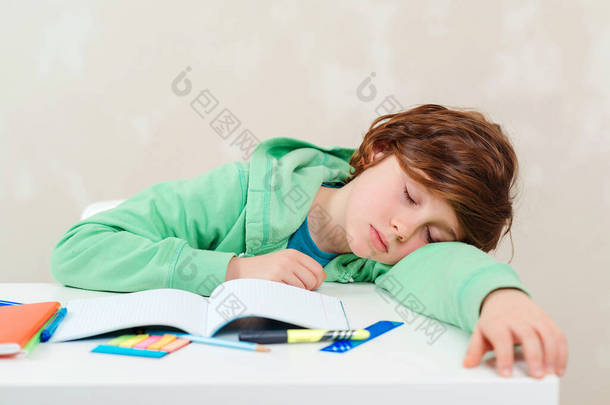 累了的学生在做作业的时候就睡在桌边。学习困难、教育、作业概念.男孩在做家庭作业。压力大又累的孩子沮丧的孩子坐在书桌前，拿着许多书.