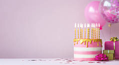 粉红色的生日蛋糕，上面有金色的蜡烛和气球