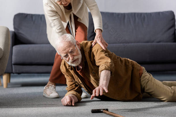 老年人躺在地板上，试图在妻子帮助他时拿起手杖