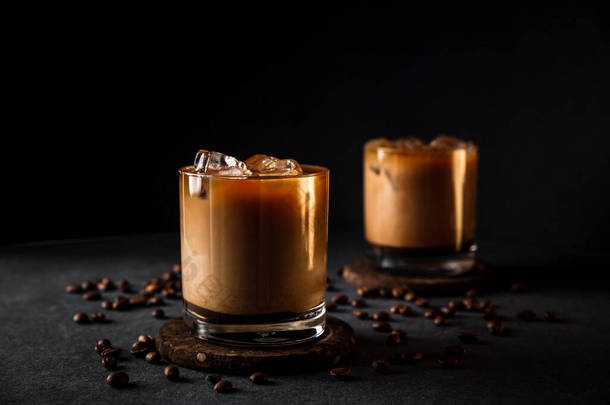一个水平的照片2个岩石眼镜与冷冰镇咖啡牛奶，咖啡豆周围，黑暗的背景，深深的阴影