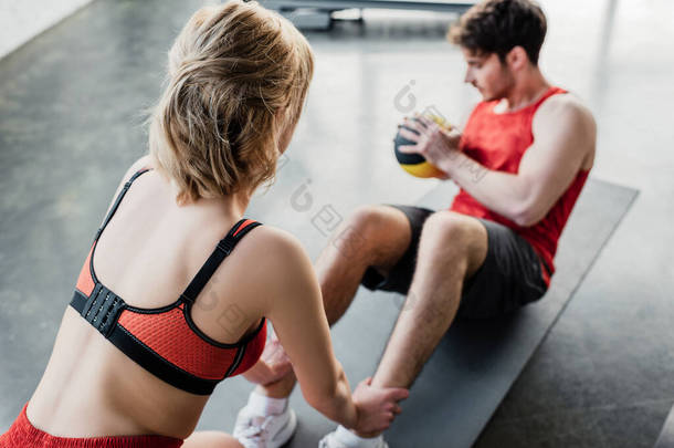 有运动能力的女子抱着运动员的腿，带着球在健身垫上运动的<strong>选择</strong>性<strong>焦点</strong>