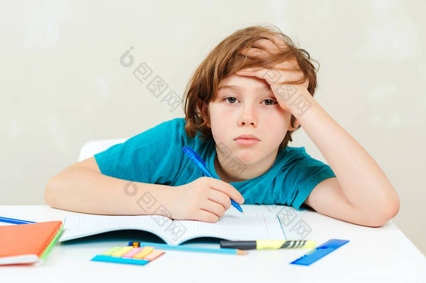 累了的学生坐在桌旁。男孩在做家庭作业。学习困难，教育观念。压力大又累的孩子灰心<strong>丧气</strong>的孩子坐在书桌前,手里拿着许多书.可怜的疲倦的学童.