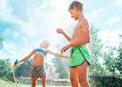 哥哥和姐姐在夏天的花园里玩浇水软管时，玩得很开心