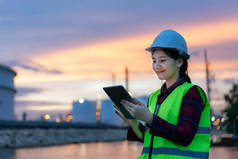 亚洲女石油化工工程师在夜间与数字平板电脑一起工作石油和天然气精炼厂内部的工厂在夜间进行检查员安全质量控制