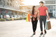 一对快乐的年轻夫妇手拿着五颜六色的购物袋，走在购物街上。售卖概念及黑色星期五购物