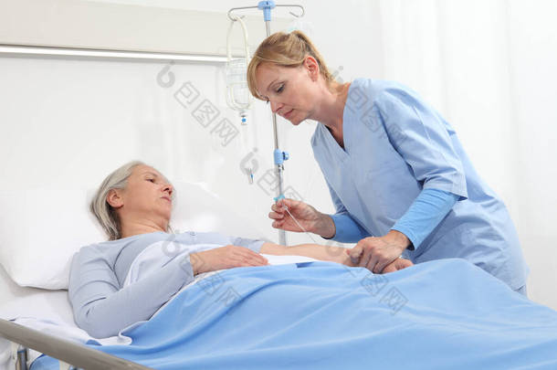 老年妇女躺在病房的病床上，护士拿着针头把静脉注射器和病人的胳膊连接起来