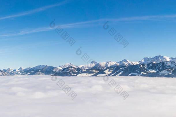 雪山山脉的壮观全景从倒置的雾层中伸出来.壮观的全景,乌云之上,阳光灿烂的蓝天.Ofterschwanger Horn, Alps, Allgau, Bavaria, Germany.