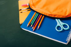 带有笔记本、彩色铅笔、画笔和剪子的绿色黑板背负式背包的高角图
