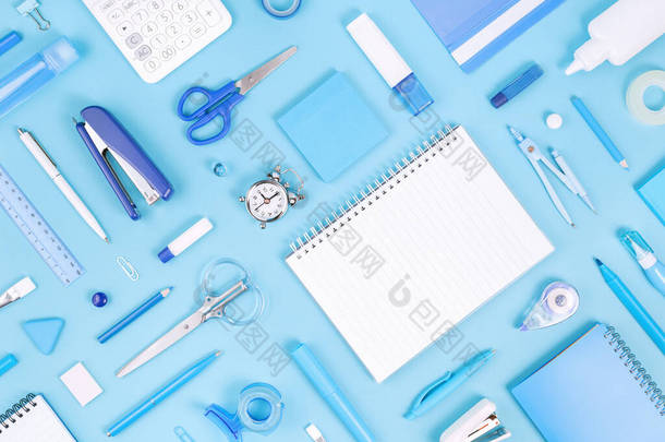 将办公室和学校的白色和蓝色文具和记事本分类，贴在胶粘的背景上。平躺在地上，有复制空间，可以回到学校或教育和手工艺的概念。蓝色单色横幅