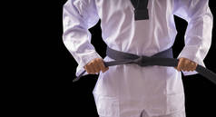 跆拳道传统男子手拿着黑色背景的黑带做广告。空手道运动员站在黑带上，与黑带隔离，并留有复制空间.