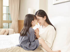 可爱的亚洲母亲和可爱的女儿坐在家里的床上