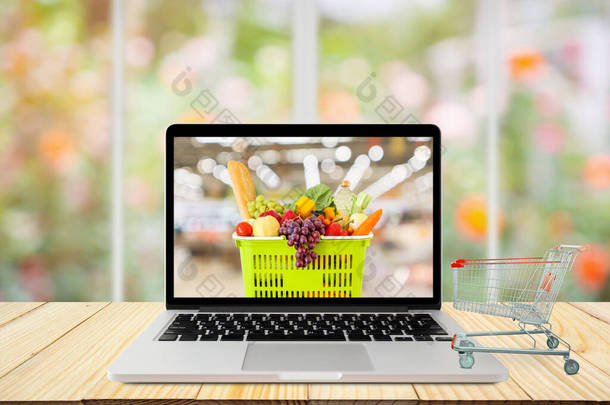 laptop computer and <strong>shopping</strong> cart on wood table with window and garden abstract blur background groc