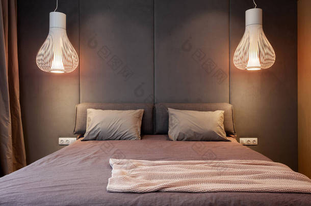 室内设计<strong>新颖</strong>的现代居室，舒适的床上点着灯光灯，床罩上有枕头，背靠着柔软的头枕