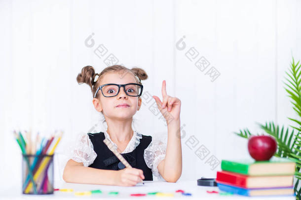 在课桌前开心地微笑着的学生指指点点.教室里的女孩拿着铅笔，书本。小学的小女孩。秋天的第一天。回学校去