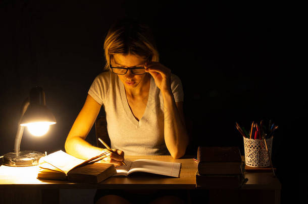 在黑暗的房间里，一个女孩坐在灯光下的桌子旁边做<strong>作业</strong>，做<strong>作业</strong>，做<strong>作业</strong>