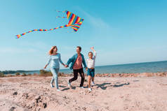 在父母近旁的海滩上，孩子们牵着风筝的选择性焦点