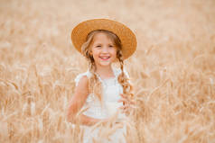 金发小女孩戴着草帽,在麦田里喝牛奶.环境友好型农产品