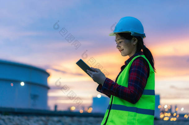 亚洲女石油化工工程师在夜间与数字平板电脑一起工作石油和天然气精炼厂内部的工厂在夜间进行检查员安全质量控制