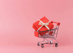 购物车红色礼品盒正面视图，粉色背景，有复制空间。圣诞假期购物概念.