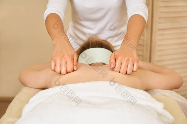 专业按摩妇女在温泉沙龙给一个年轻女孩做背部按摩，近距离按摩按摩师的工作。专业按摩的概念。身体护理概念.
