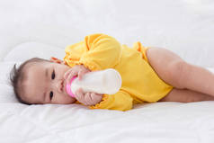 一个亚洲婴儿睡在床上，正在吸瓶装奶.