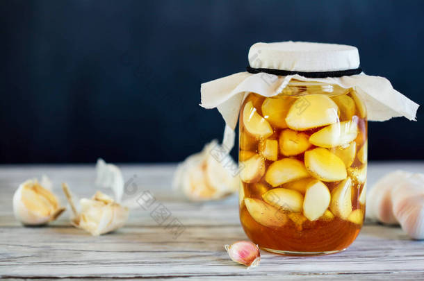 发酵大蒜丁香在蜂蜜瓶，一个丰富的益生菌来源，在一个乡村木材背景表。背景和前景模糊的选择性重点.