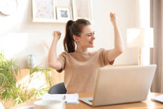 快乐的女企业家坐到桌旁，高举双手，读着好消息，表达喜悦