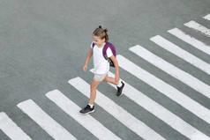 女学生在去学校的路上过马路。斑马的交通走在城市的路上。过人行横道的概念行人。时髦的少女背着背包走着。活跃的孩子。顶部视图