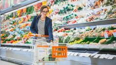 在超级市场：漂亮的年轻女人在购物车里放杂货。在商店的新鲜农产品区买蔬菜的女售货员.