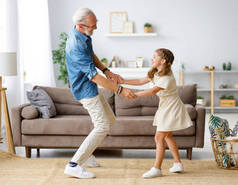快乐的家庭：女孩站在舒适的客厅里的沙发上，与年老的祖父一起笑着跳舞