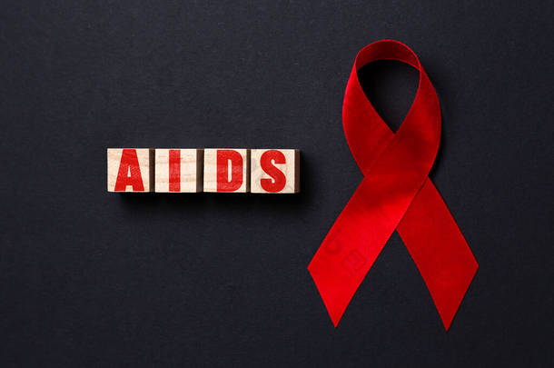 红色缎带和木制立方体与字艾滋病在黑色背景。靠近点平躺在床上世界艾滋病日的概念.
