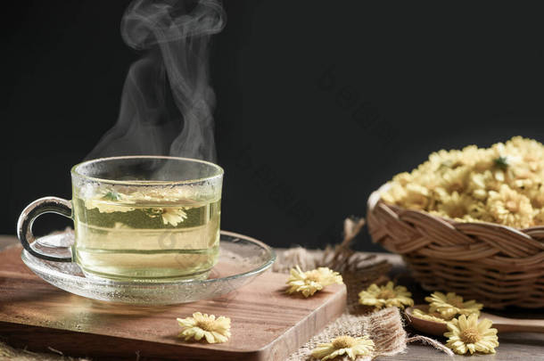 菊花茶与热蒸汽和菊花在篮子里的黑色背景。健康的饮料狂怒。草药和医疗概念.