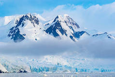 南极洲被白云覆盖的白雪覆盖的高山。美丽的冰川