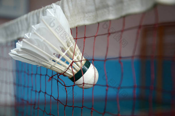 羽毛球羽毛球卡在网子上.白色羽毛球和红色羽毛球网，背景模糊