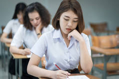 选择重点的青少年大学生坐在讲座椅子上做期末考试，并在课堂上填写试卷答题单。在教室里穿制服的大学生.
