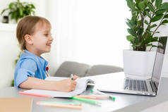 可爱的小女孩带着她的笔记本电脑坐在桌旁，在网上学习