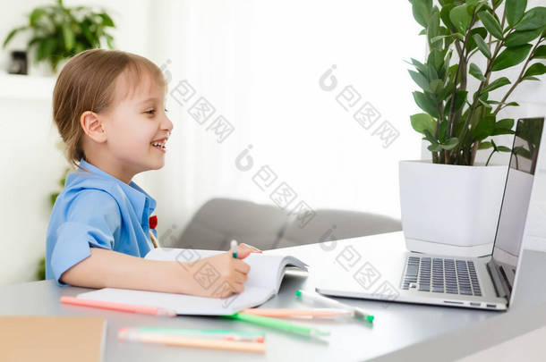 可爱的小女孩带着她的笔记本电脑坐在桌旁，在<strong>网上学习</strong>