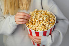 一个准备看电影的小女孩手里拿着爆米花纸桶。表演时间到了吃美味的不健康的甜食.去电影院看一部新电影。休息和娱乐。爆米花特写