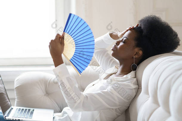 患有<strong>中暑</strong>的非洲女商人坐在家里客厅里挥动扇子