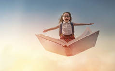 回学校去！快乐可爱的勤劳的孩子在夕阳的背景下在书上飞翔.教育和阅读的概念。想象力的发展.