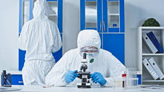 穿危险物品套装的科学家在实验室与显微镜同事一起工作