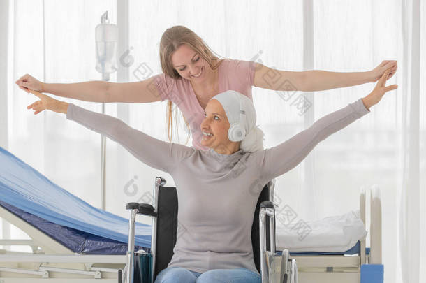 一位坐在轮椅上的中年乳腺癌患者和她的女儿张开双手，自由而快乐。家庭支助和鼓励生病人员的想法.