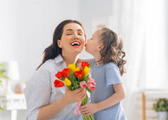 母亲节快乐。小女儿向妈妈表示祝贺,并送给她鲜花.妈妈和女孩笑着和拥抱。家庭假日和团聚.